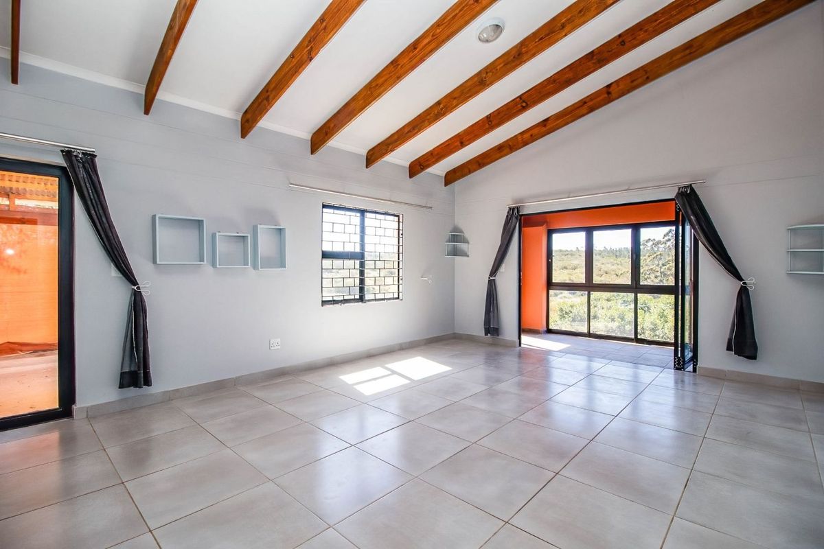 Spacious living area featuring vaulted ceilings with exposed timber beams, large format floor tiles, and expansive glass sliding doors opening to an outdoor space.
