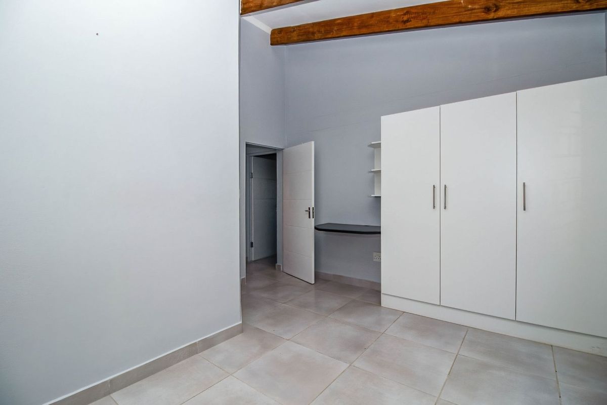 A bedroom featuring tiled flooring, built-in white wardrobes, a small integrated desk, and exposed timber ceiling beams.