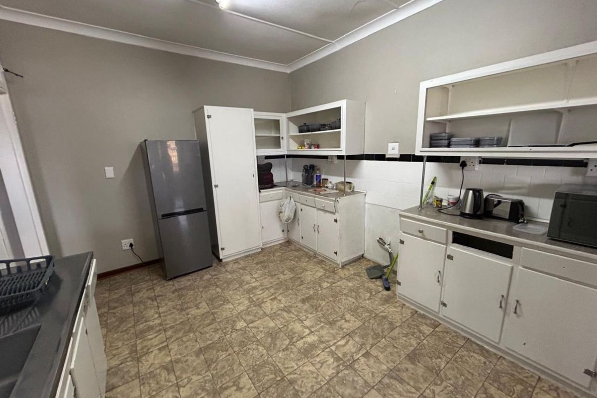 A dated kitchen featuring white cabinetry, tiled flooring, and basic laminate countertops, offering a functional space with potential for modernization.