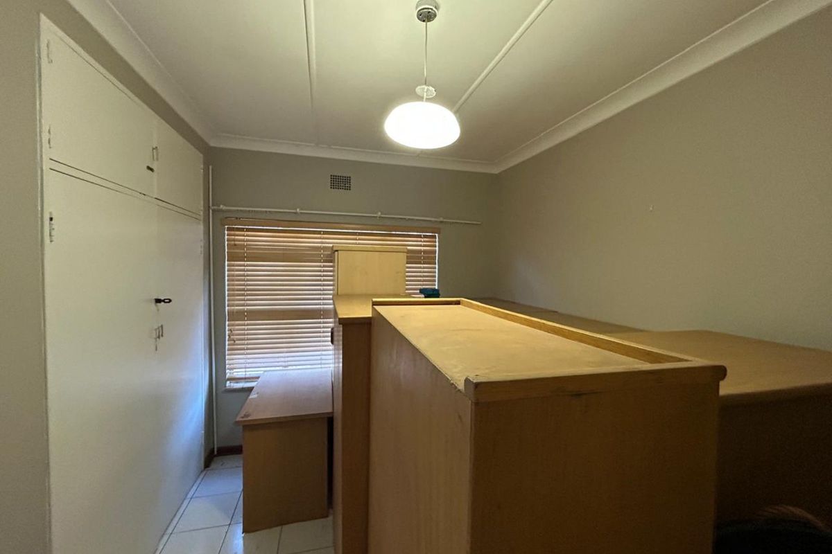 A bedroom featuring built-in cupboards, tiled flooring, and a window with fitted blinds.