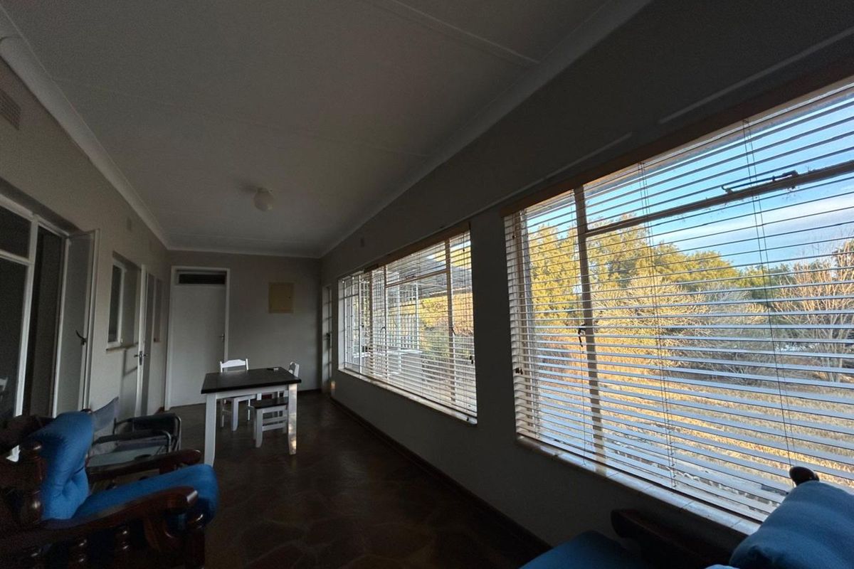 A sun-filled living area featuring large windows with fitted blinds, tiled flooring, and neutral wall finishes, offering a bright and functional space.