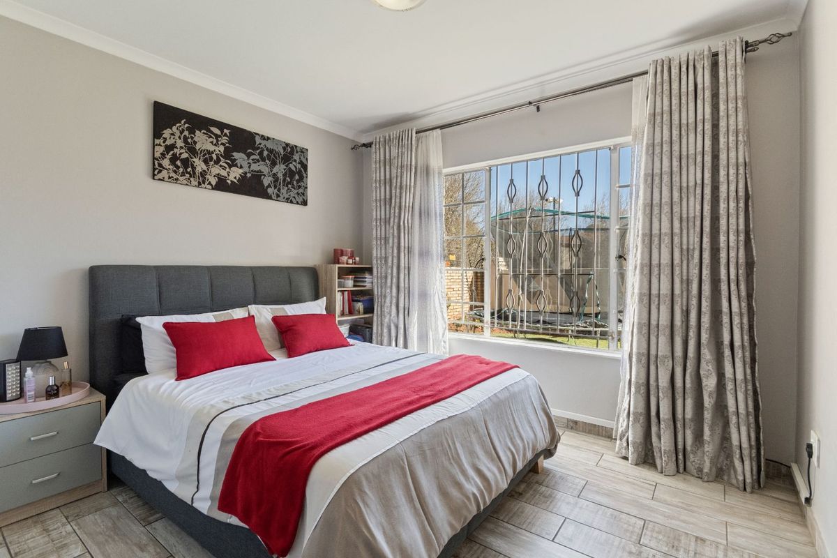 A well-lit bedroom featuring tiled flooring, large window with security bars, and neutral wall finishes.