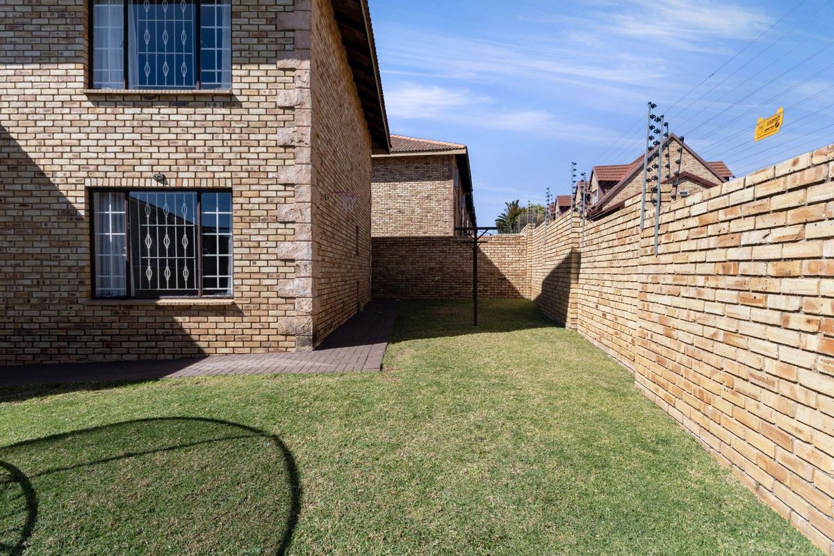 A private rear garden area featuring face-brick boundary walls, security electric fencing, and a paved walkway adjacent to the townhouse structure.