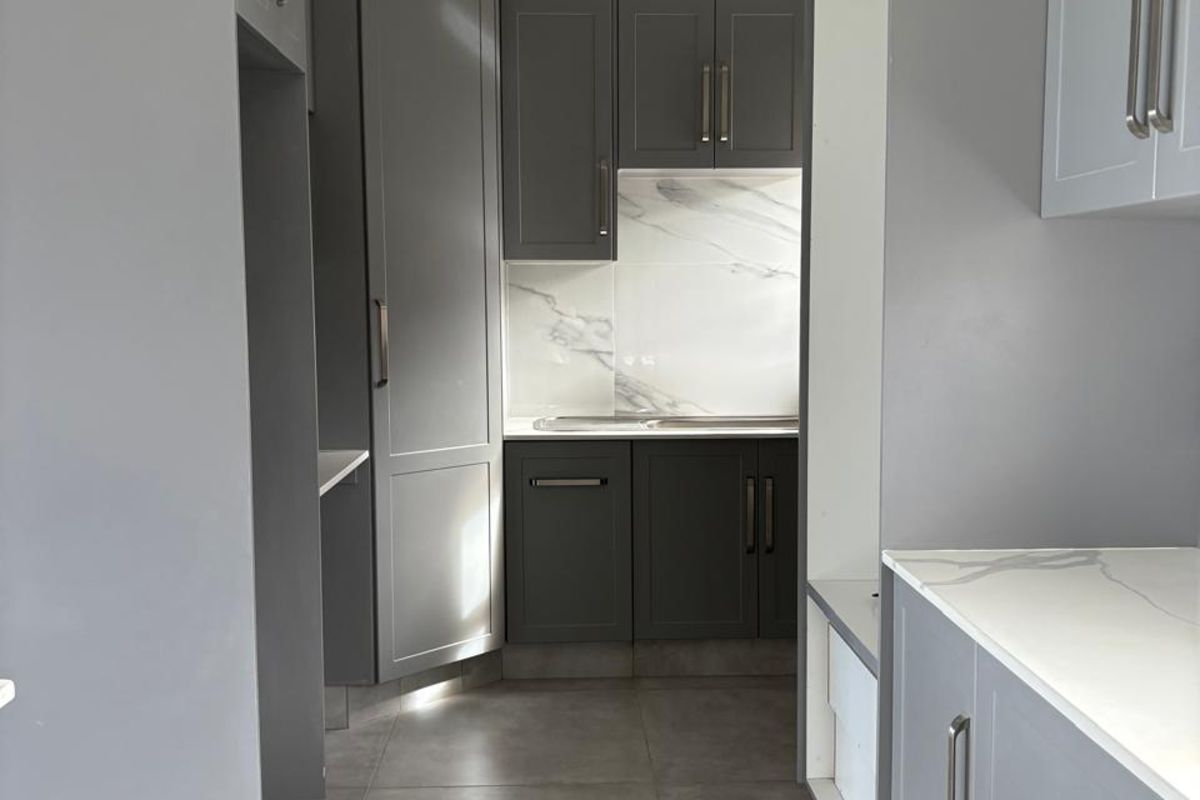 Modern kitchen featuring grey shaker-style cabinetry, marble-look splashback, stone countertops, and large format floor tiles.