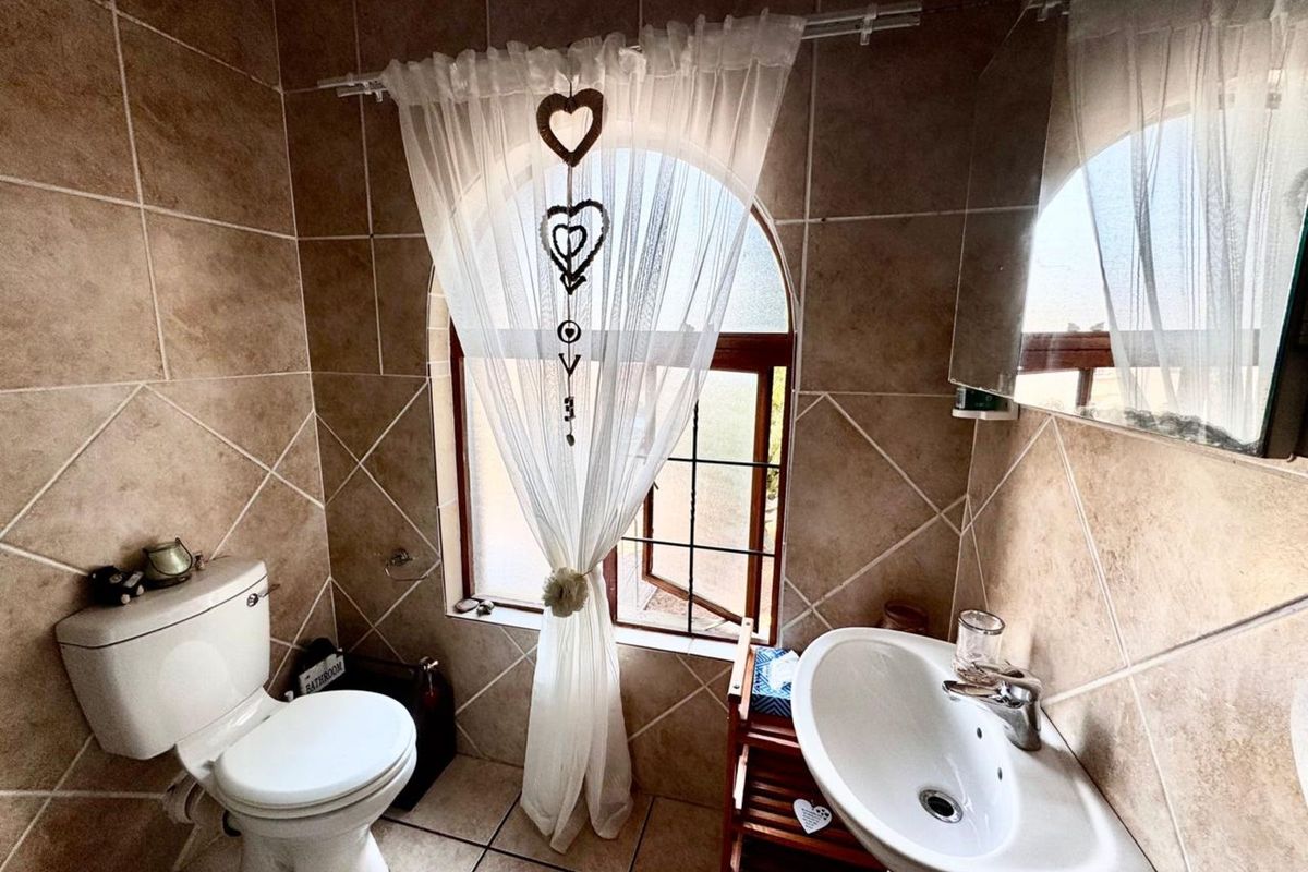 A compact bathroom featuring floor-to-ceiling ceramic tiling, a pedestal basin, and a toilet, illuminated by a distinctive arched window.