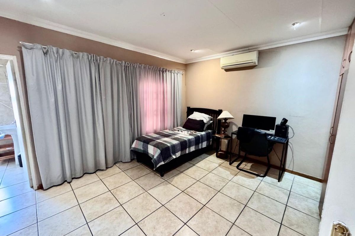 A bedroom featuring tiled flooring, built-in cupboards, and a wall-mounted air conditioning unit.