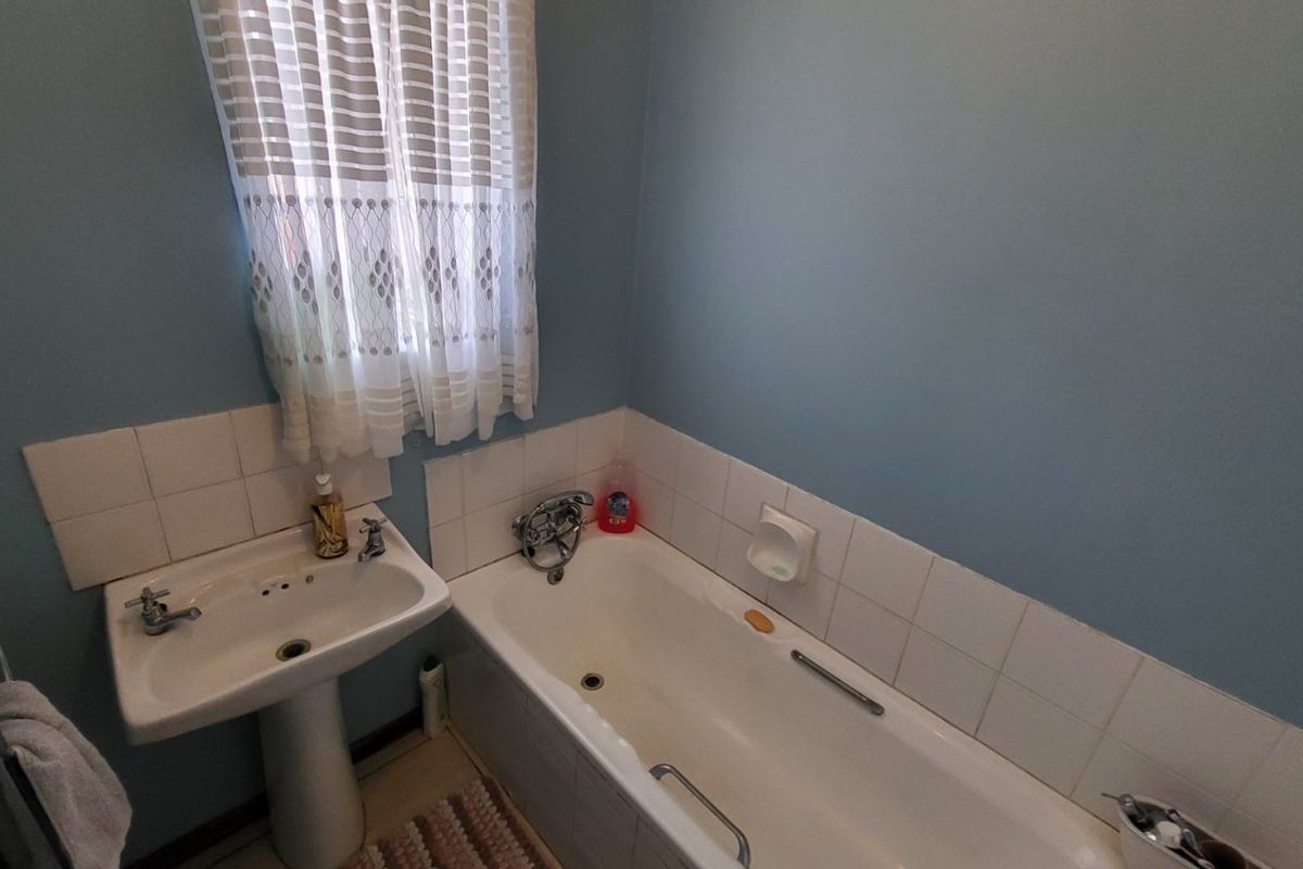 A functional bathroom featuring a pedestal basin, a standard bathtub with integrated grab rails, and tiled splashbacks.