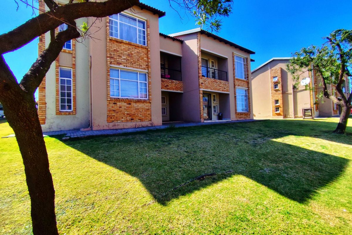 A view of the apartment complex exterior featuring brick and plaster facade, multi-level balconies, and well-maintained surrounding lawn area.