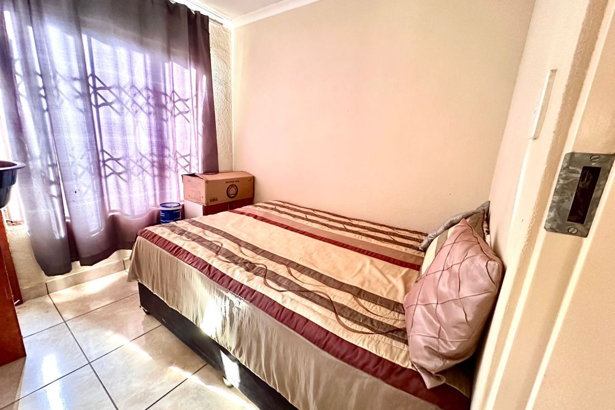 A compact bedroom featuring tiled flooring and a window with security bars, providing a functional space for a single bed.
