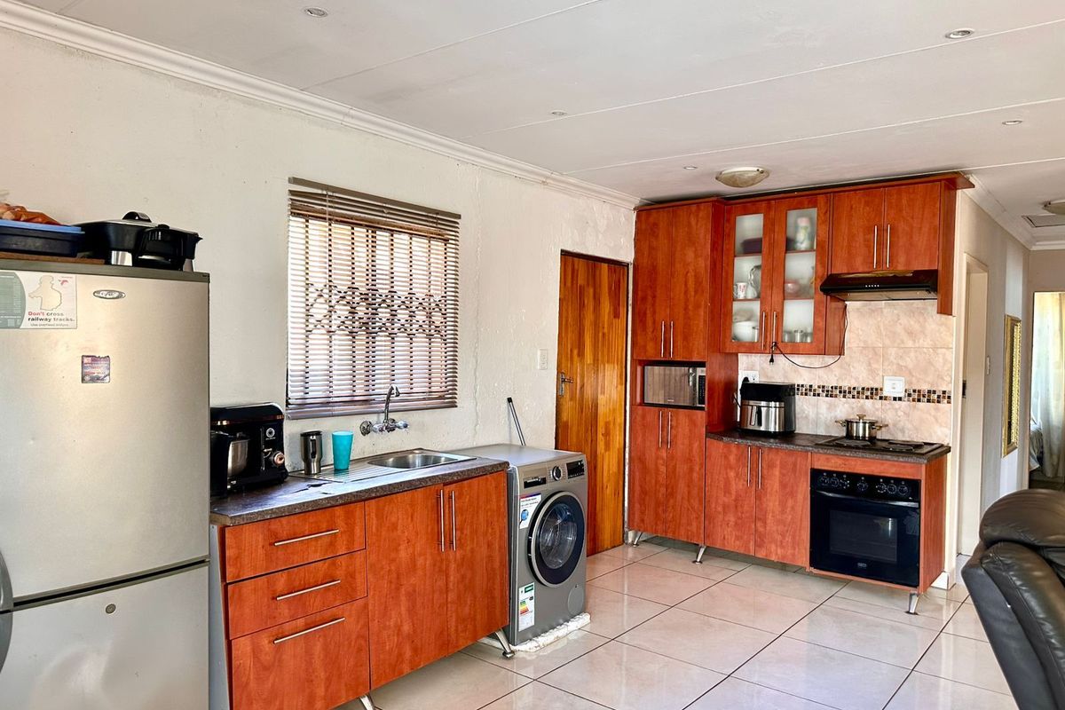 Functional kitchen featuring wood-look cabinetry, built-in oven, hob, extractor fan, and integrated laundry plumbing, finished with tiled flooring and tiled splashbacks.