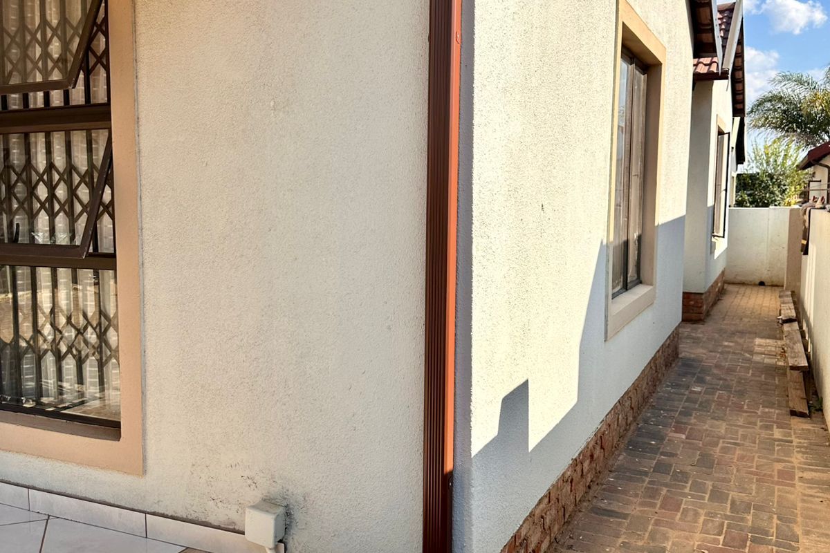 Side exterior view of the house featuring paved walkway, plastered walls, and metal security bars on windows.