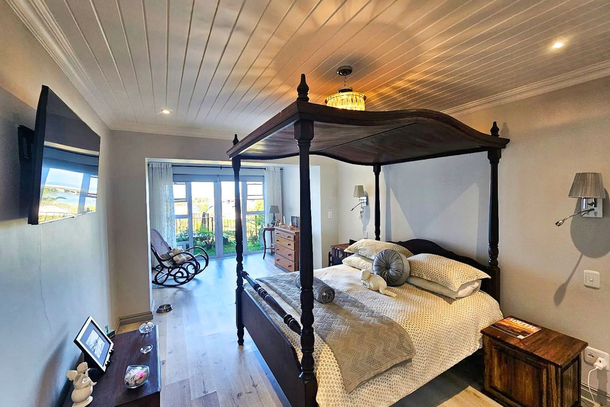 Spacious bedroom featuring a four-poster bed, light wood-look flooring, tongue-and-groove ceiling, and sliding glass doors leading to an outdoor balcony area.