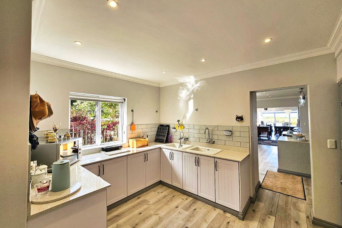 A functional kitchen featuring light-toned cabinetry, stone-look countertops, subway tile backsplash, and wood-look flooring, with a view into the adjacent living area.