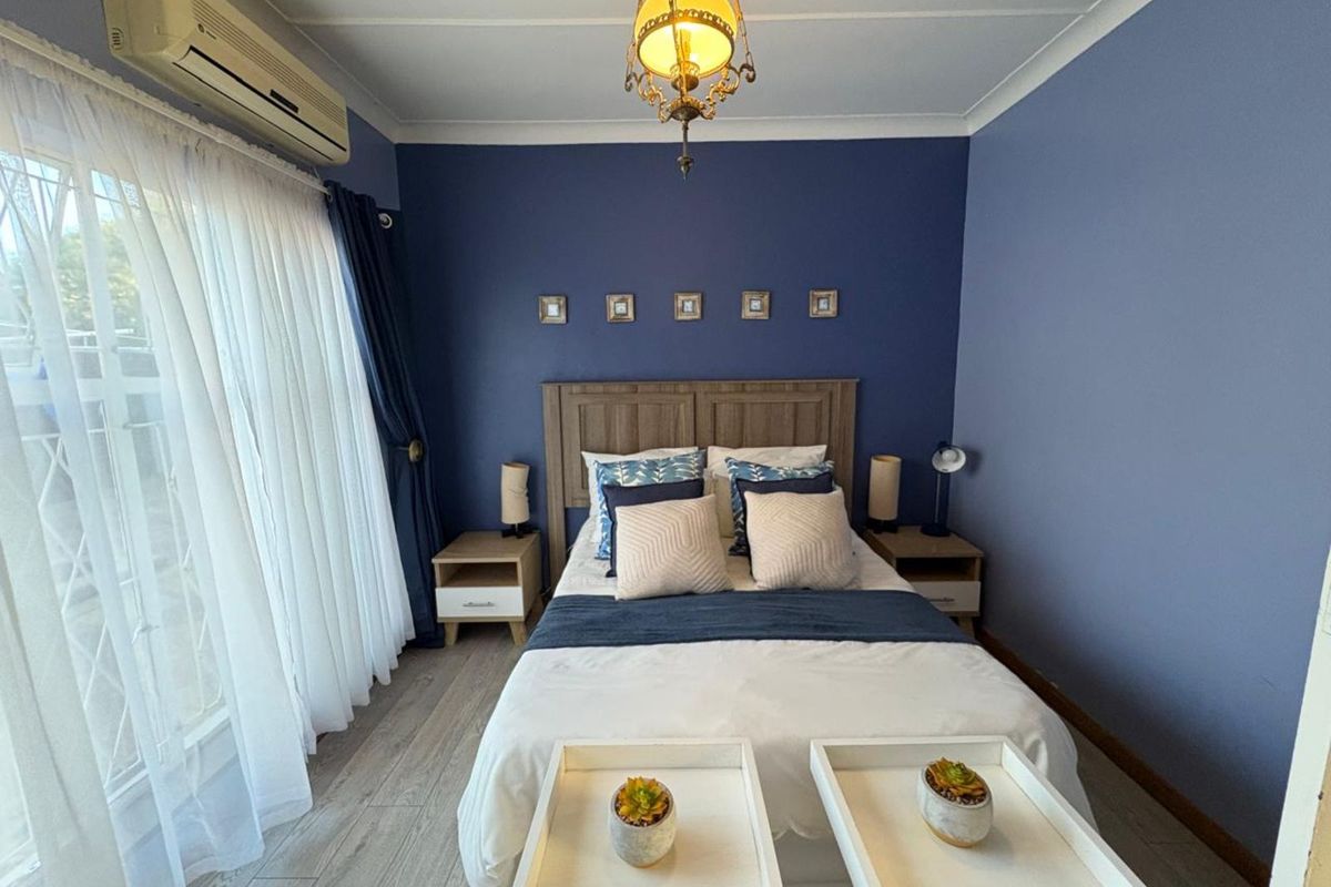A well-maintained bedroom featuring wood-look flooring, a split-system air conditioning unit, and a feature wall.