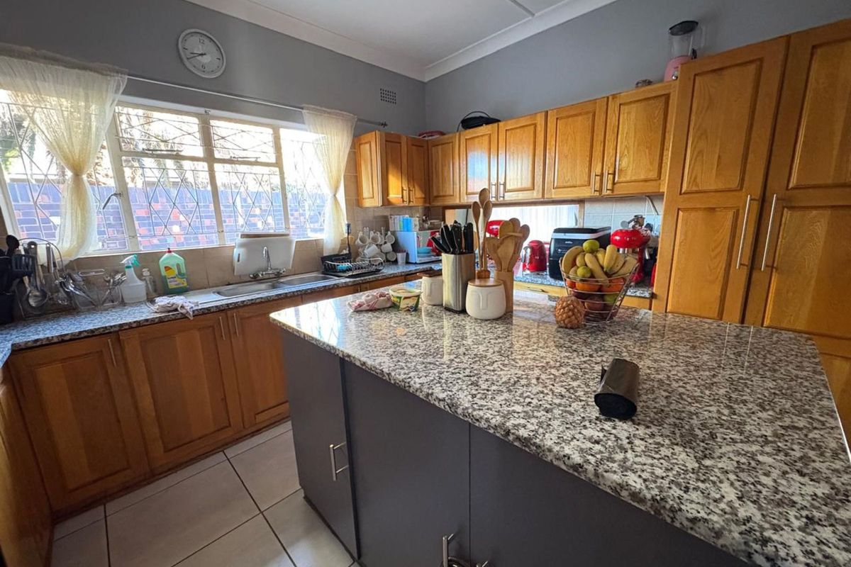 A functional kitchen featuring wooden cabinetry, granite countertops, a central island, and tiled flooring, offering ample workspace and storage.
