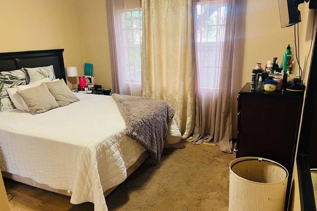 A standard bedroom featuring neutral wall tones, carpeted flooring, and large windows dressed with curtains, providing a functional and comfortable living space.