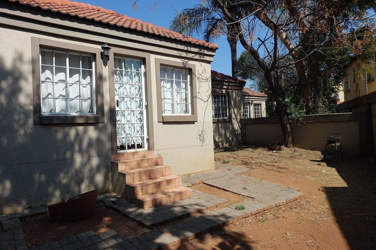 Rear view of the townhouse featuring a tiled patio, security gate, and private garden area with perimeter walling.