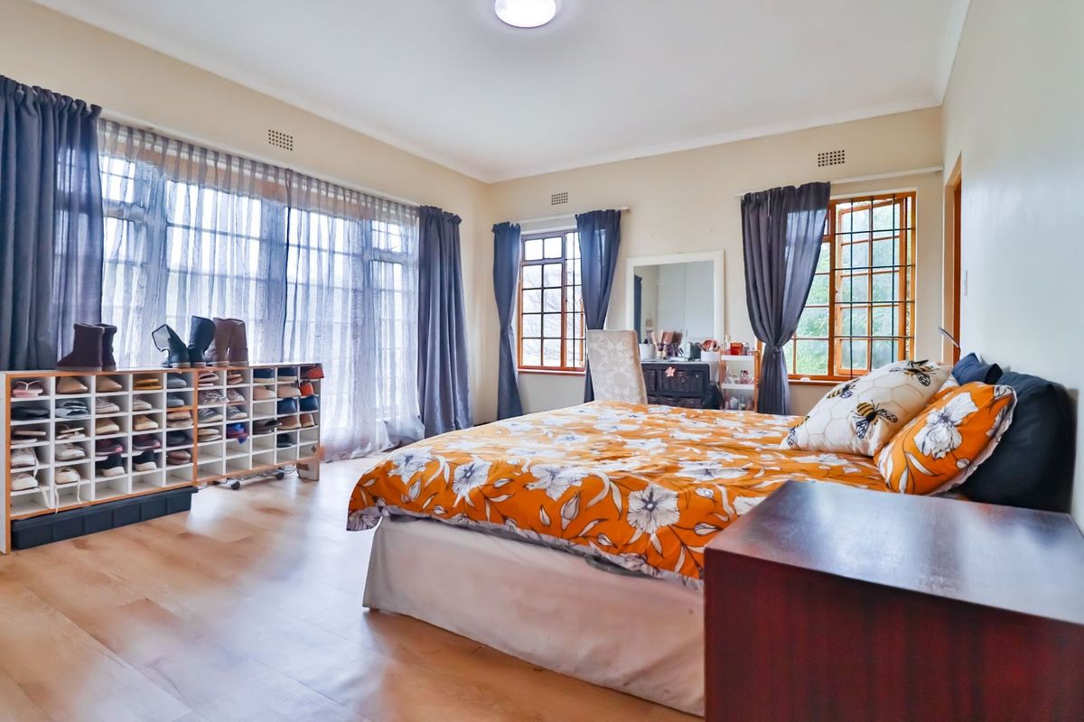 Spacious bedroom featuring large windows with wooden frames, laminate flooring, and neutral wall finishes, offering ample natural light.