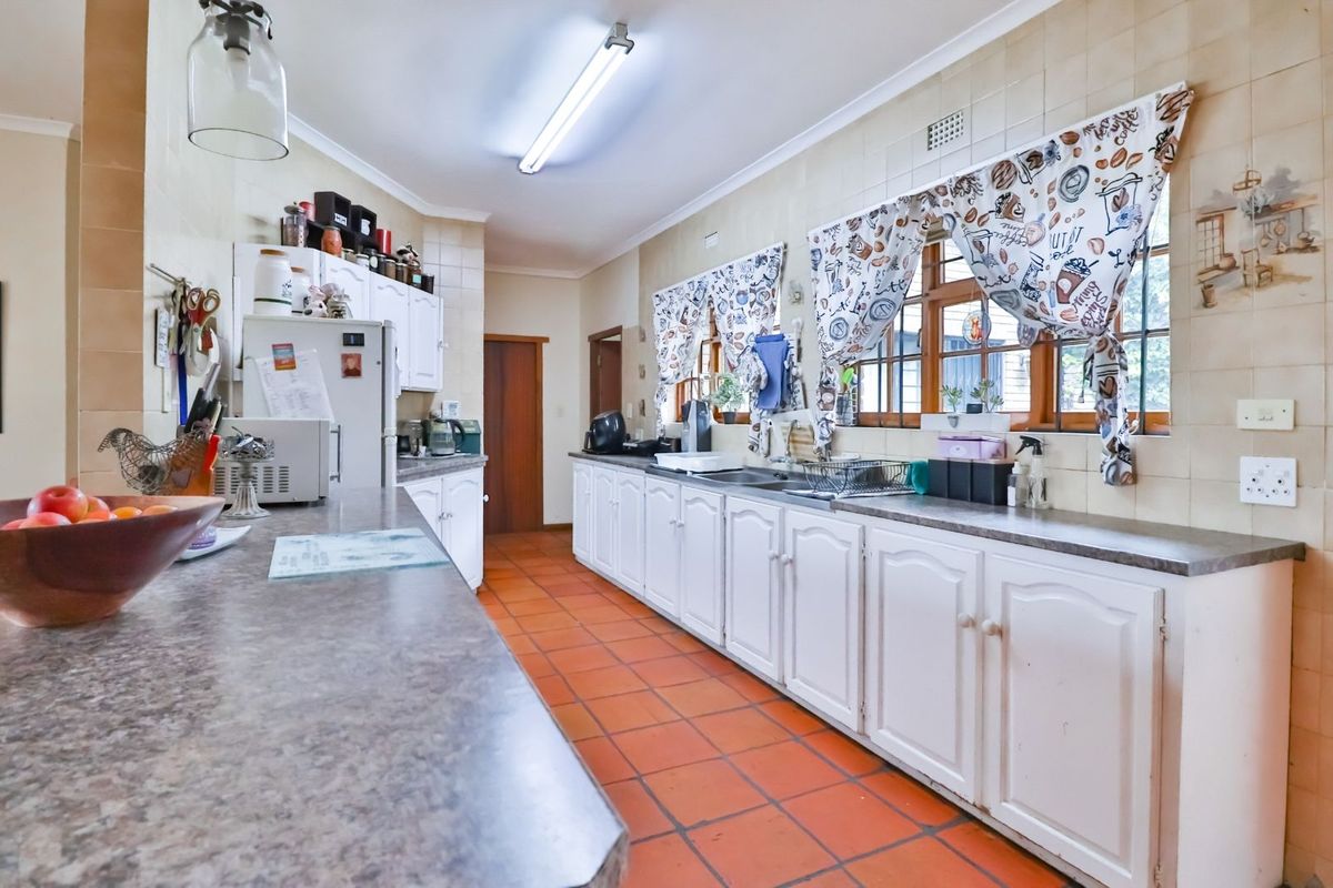 A functional kitchen featuring white cabinetry, laminate countertops, terracotta floor tiles, and tiled wall splashbacks with ample natural light.