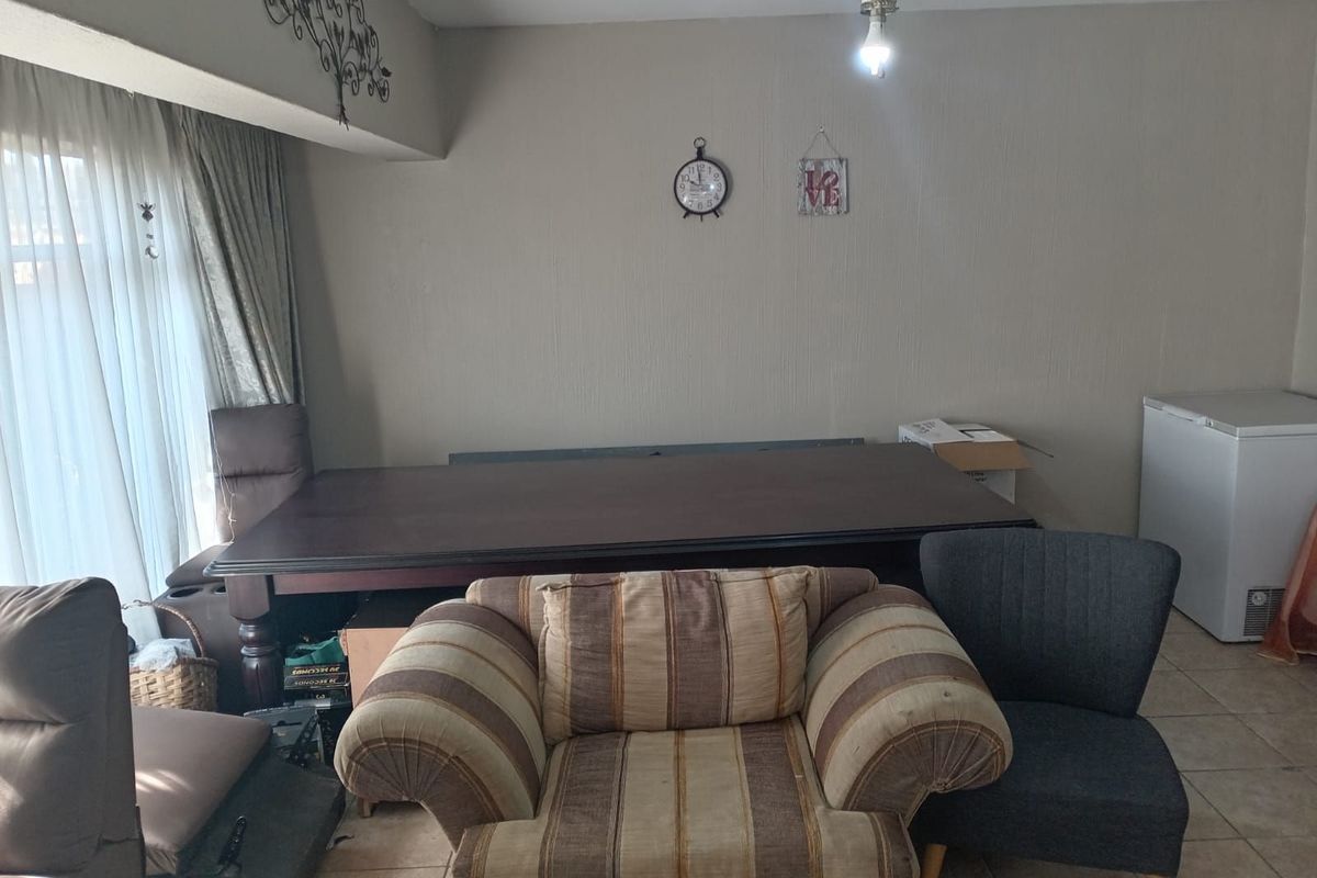 A living area featuring tiled flooring, a ceiling fan, and large windows with curtains, offering a functional space for relaxation.