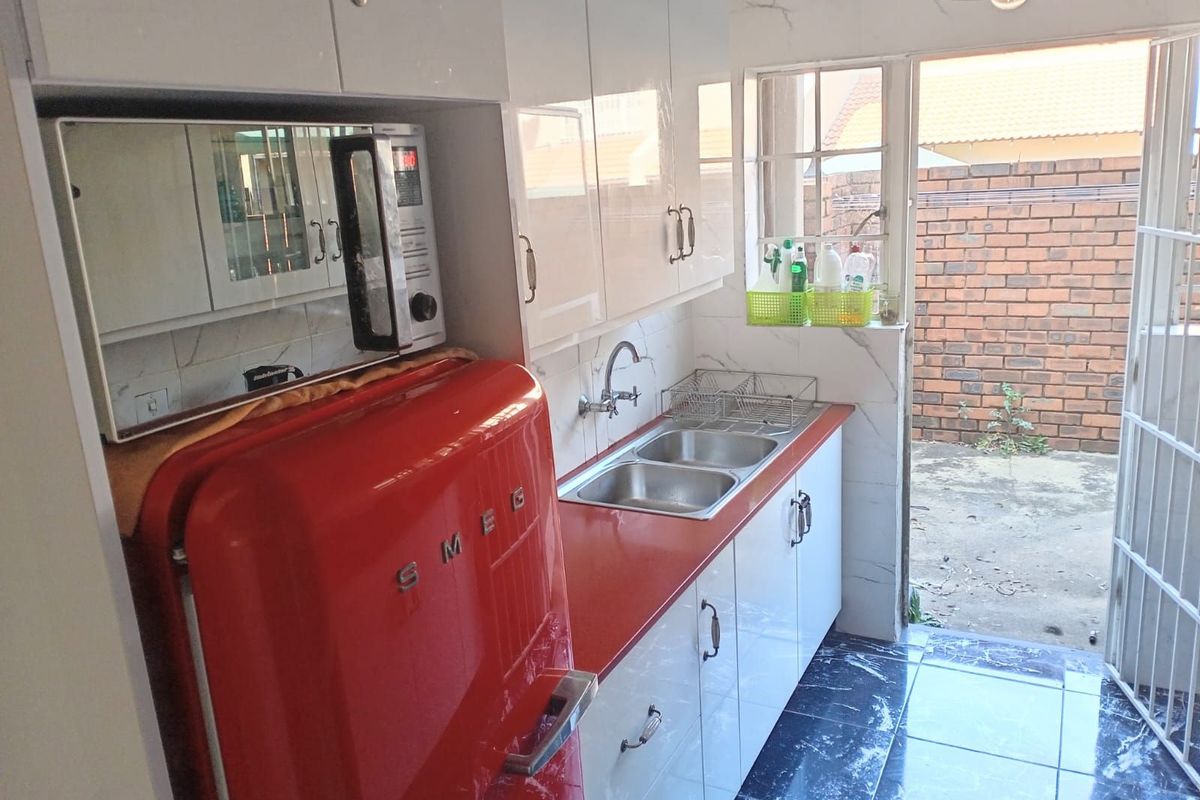 Compact kitchen featuring white cabinetry, a double stainless steel sink, and direct access to the rear exterior area.
