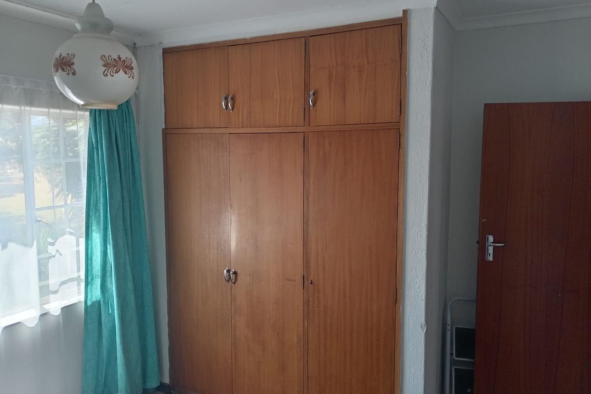 A bedroom featuring built-in wooden cupboards with overhead storage and a window providing natural light.