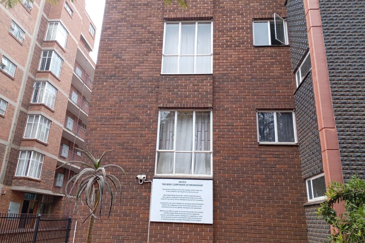 Exterior view of a multi-story brick apartment building featuring standard window configurations and a mounted security camera.