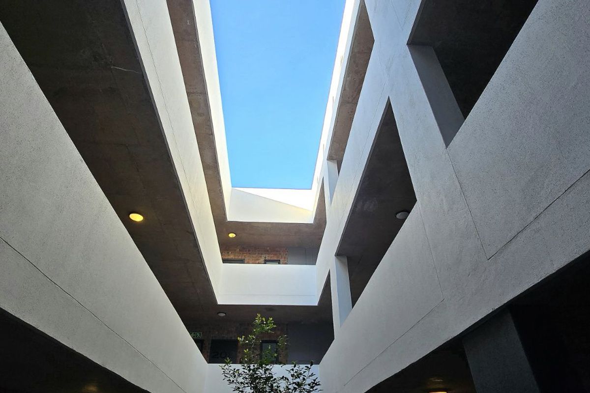A view looking up through the central atrium of a modern apartment complex, showcasing architectural concrete design and open-air circulation.