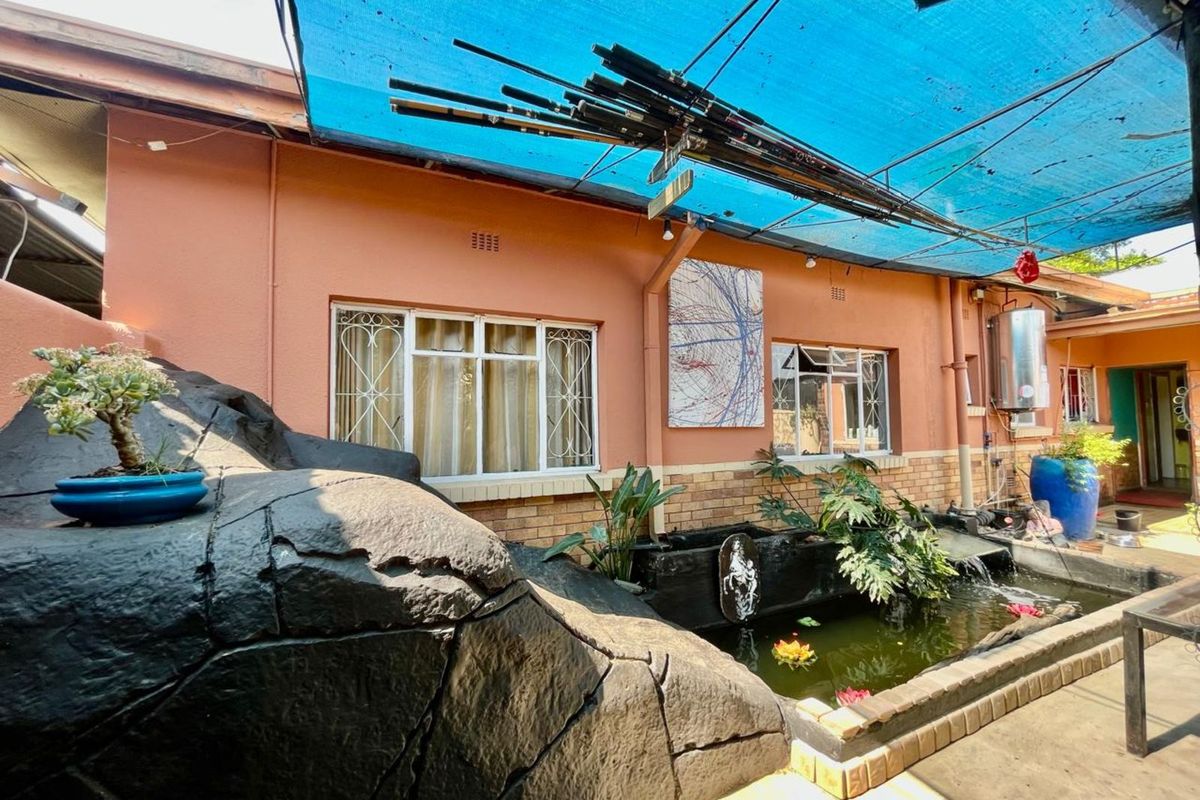 Rear patio area featuring a built-in water feature, rockery, and overhead shade structure attached to the main house exterior.