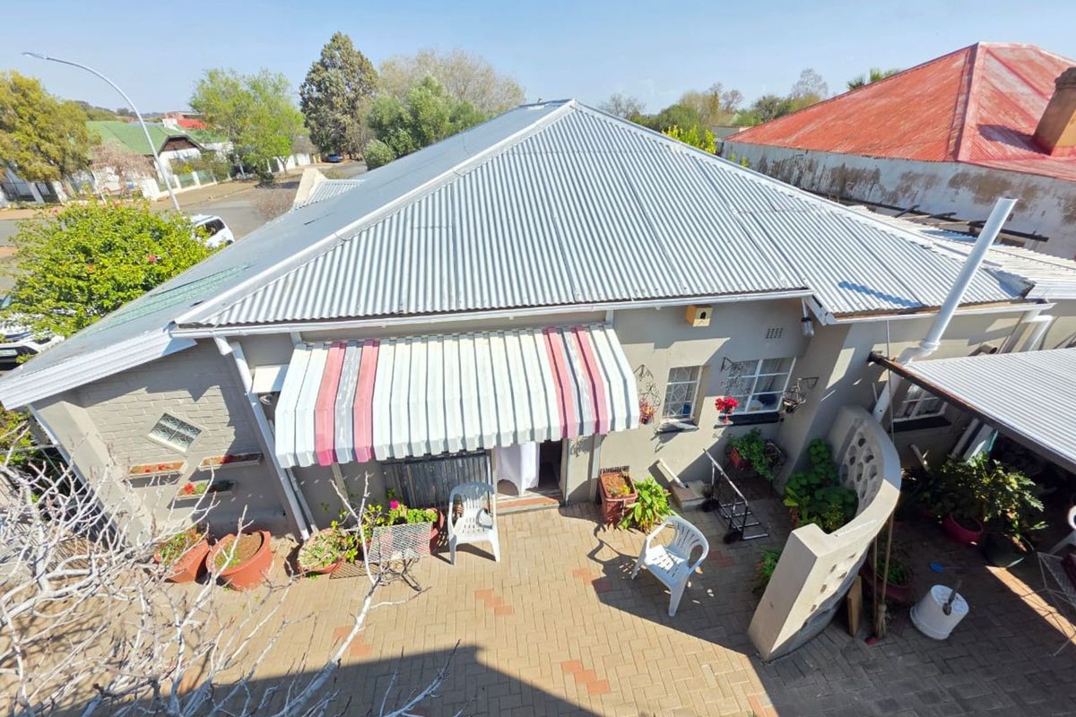 Elevated view of the rear exterior featuring a paved courtyard, corrugated metal roof, and a retractable striped awning over the entrance.