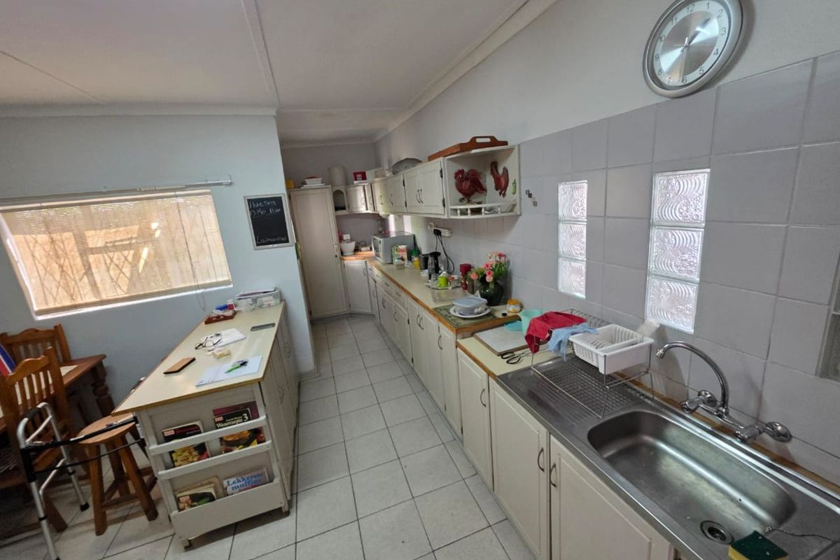 A functional kitchen featuring tiled flooring, laminate countertops, a stainless steel sink, and ample built-in cabinetry with a neutral color palette.