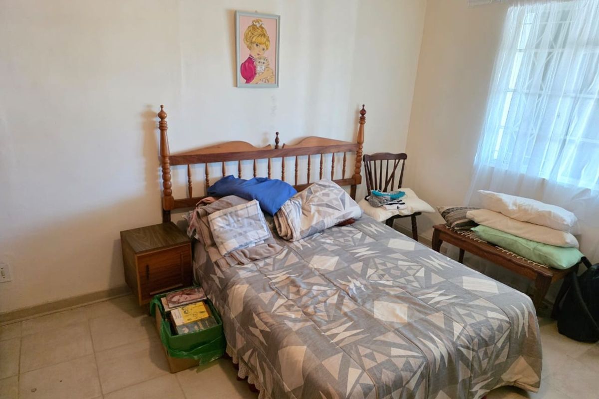 A functional bedroom featuring tiled flooring, a window with security bars, and neutral wall finishes.