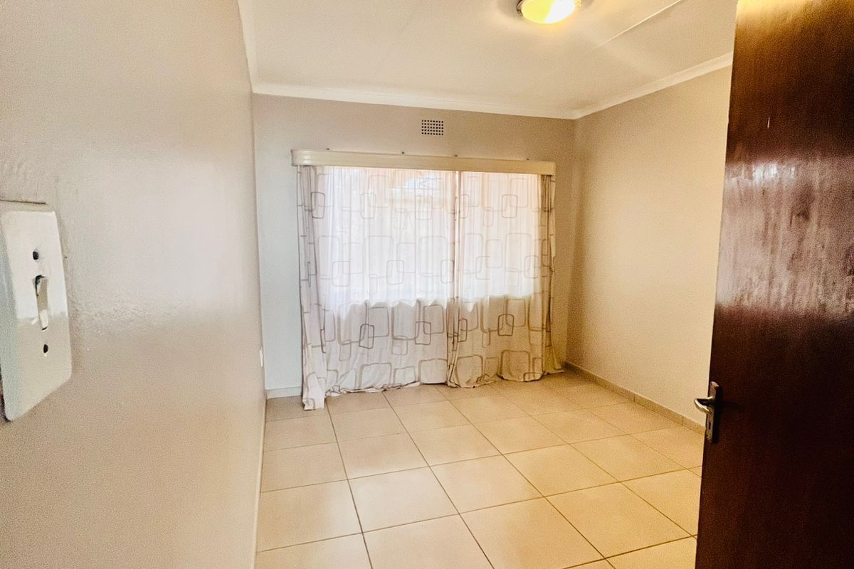 A clean, empty bedroom featuring neutral tiled flooring, a ceiling light fixture, and a window with curtain tracks.