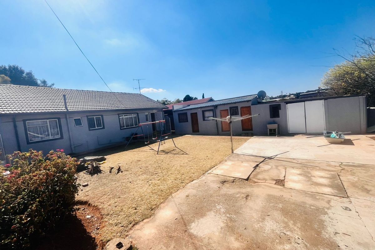 A spacious rear garden area featuring a concrete patio, lawn, and access to multiple exterior doors and outbuildings.