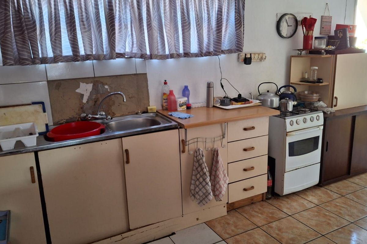A functional kitchen area featuring a stainless steel sink, built-in cabinetry, and a freestanding stove, requiring cosmetic updates to modernize the space.