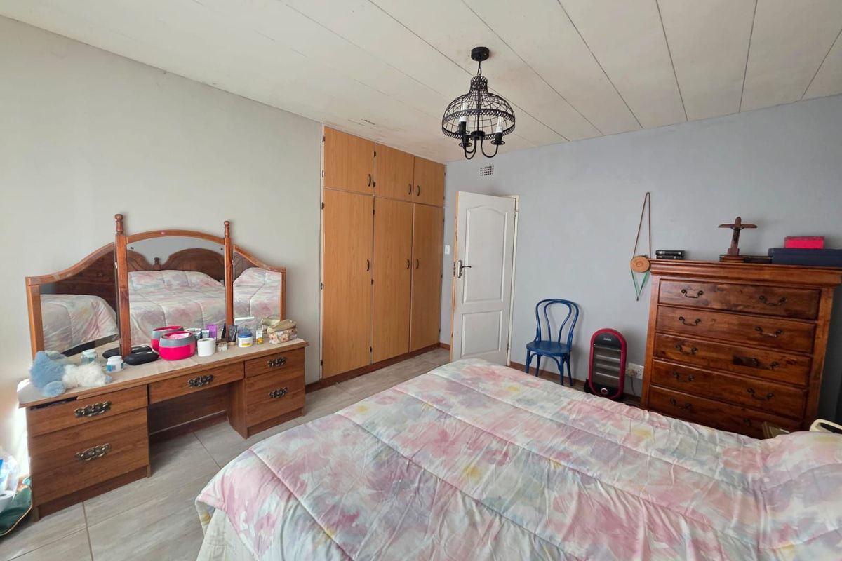 A bedroom featuring built-in wooden cupboards, tiled flooring, and a panelled ceiling.
