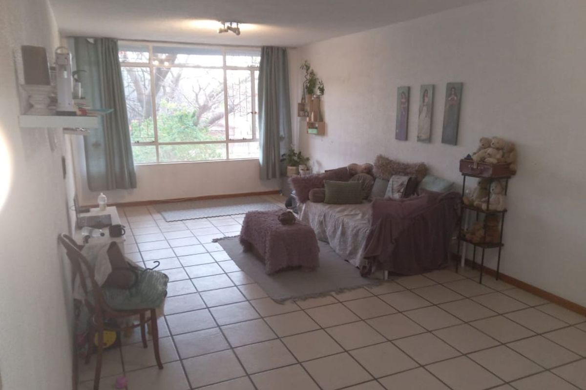 A spacious living room featuring large windows that provide natural light and tiled flooring throughout.