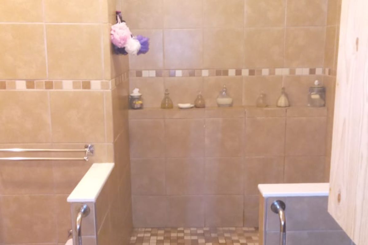 A walk-in shower area featuring beige wall tiles, a mosaic tile floor, and built-in grab rails for accessibility.