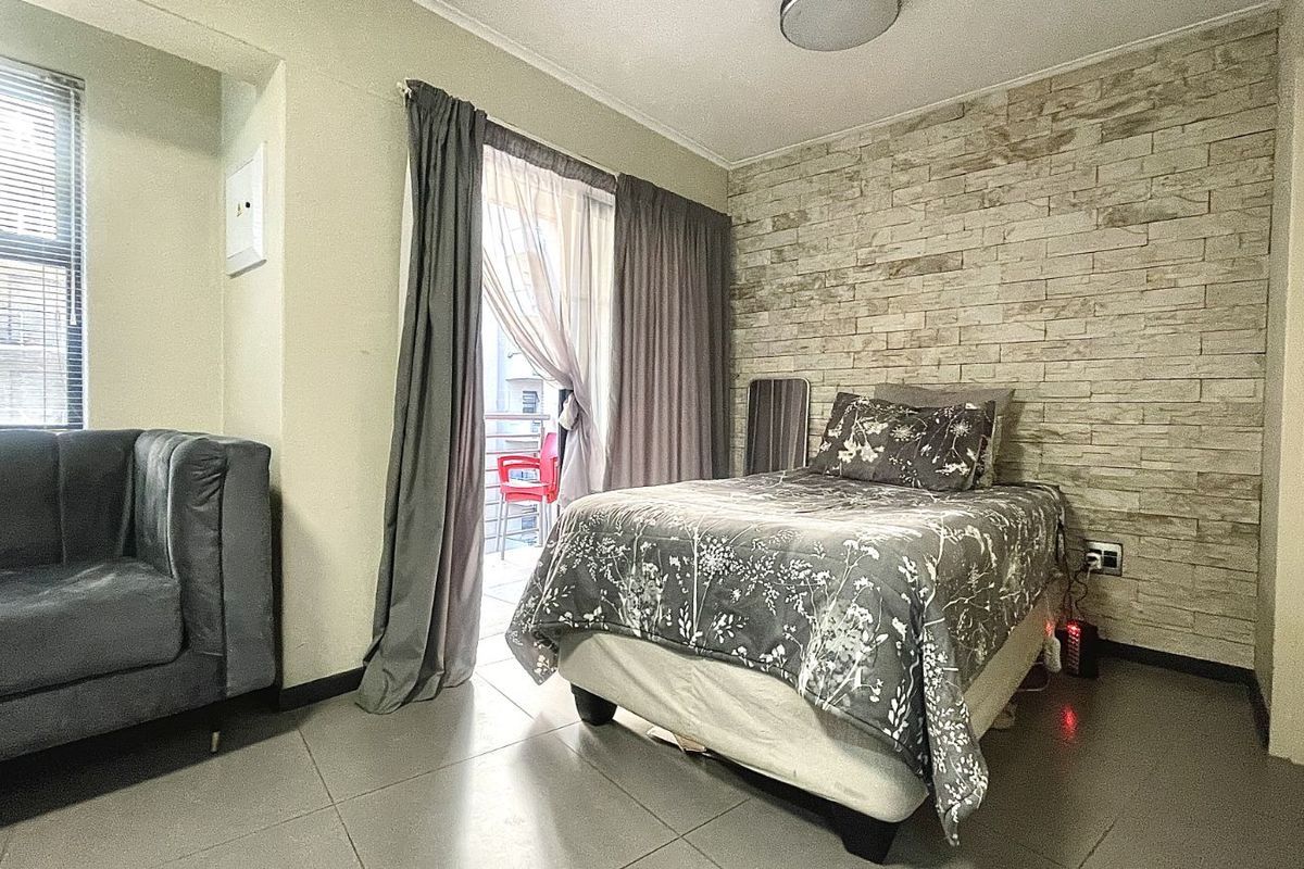 A bedroom featuring a stone-cladding accent wall, tiled flooring, and direct access to a private balcony through a sliding glass door.