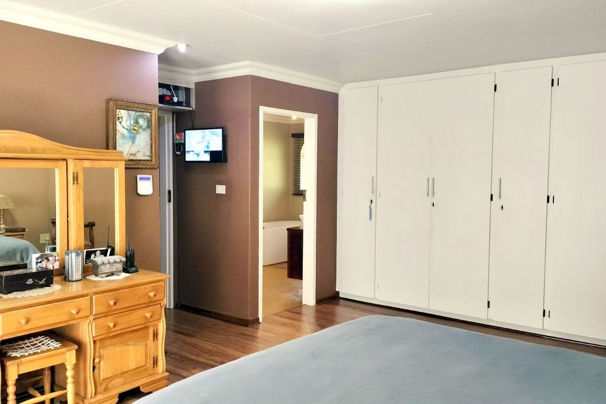 Spacious bedroom featuring extensive built-in white cabinetry, laminate flooring, and direct access to an en-suite bathroom.