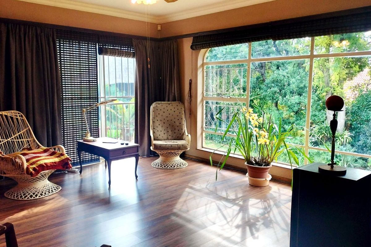 A bright living room featuring large windows with garden views, wood-look flooring, and sliding door access to an outdoor area.