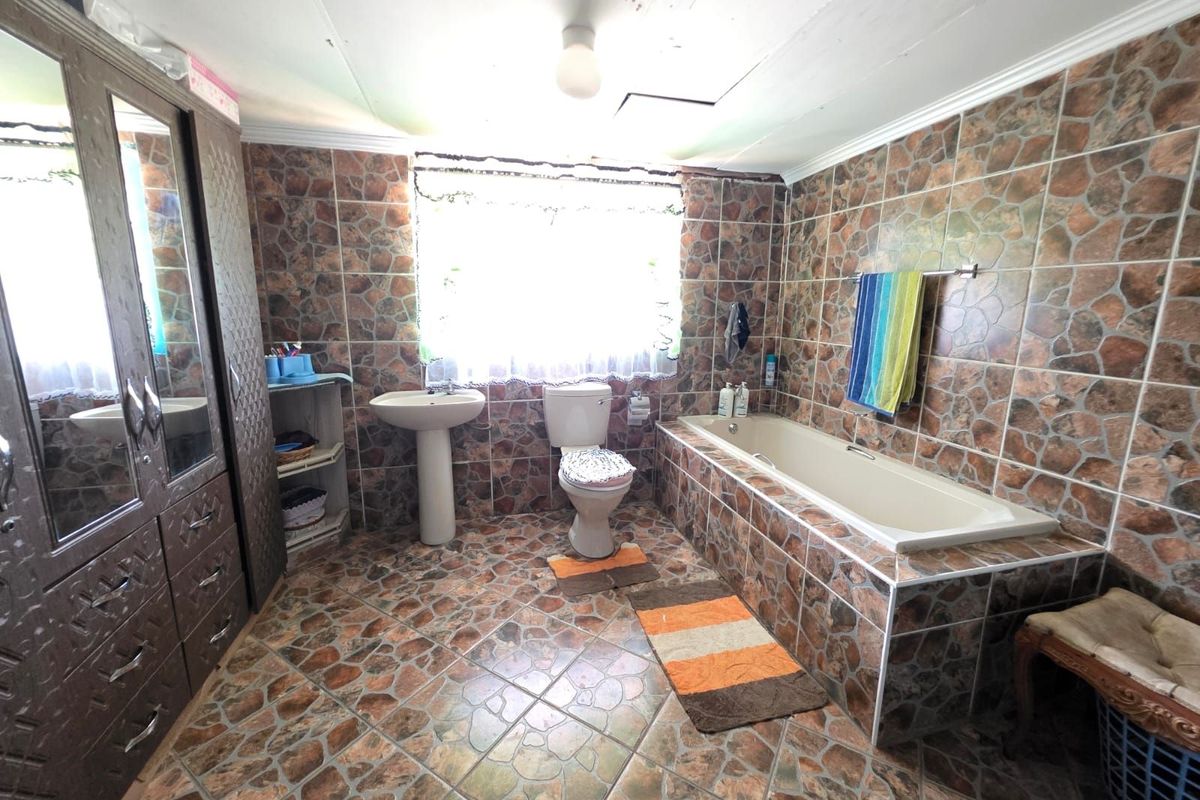 A dated bathroom featuring full-height stone-effect wall tiles, matching floor tiles, a pedestal basin, a standard toilet, and a built-in bathtub.