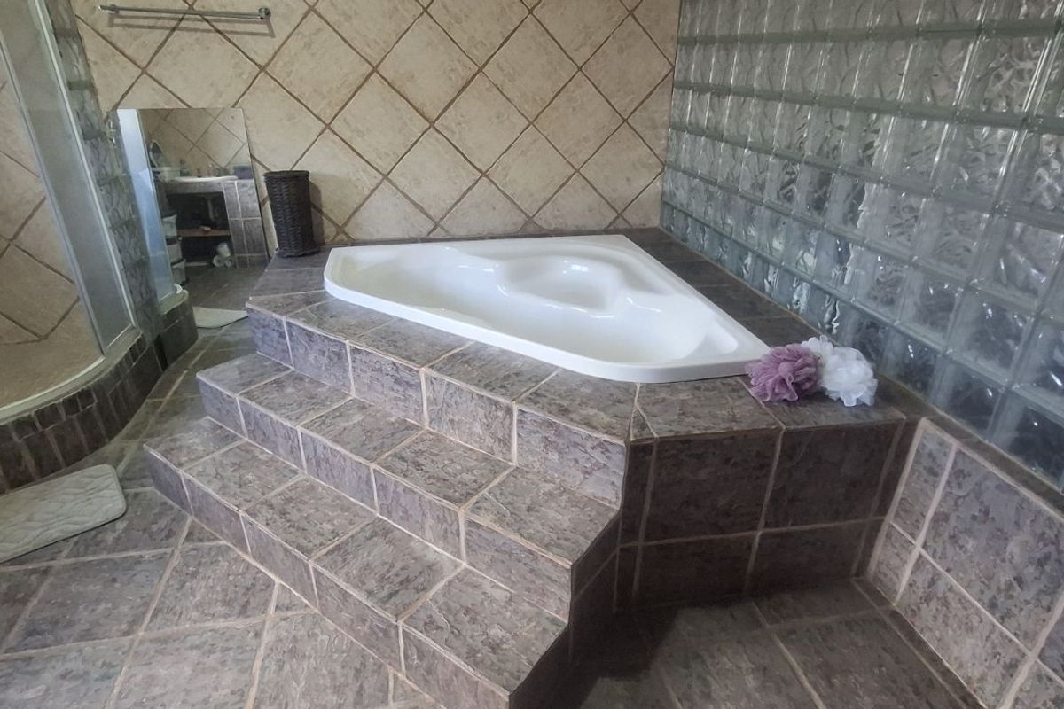A bathroom featuring a raised corner bathtub with tiled steps, a separate glass-enclosed shower, and a glass block feature wall.