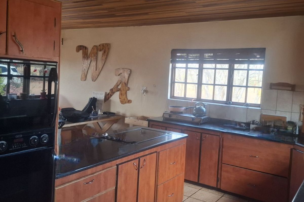 A functional kitchen featuring wooden cabinetry, dark countertops, a built-in oven, and a timber-paneled ceiling with natural light from a window.
