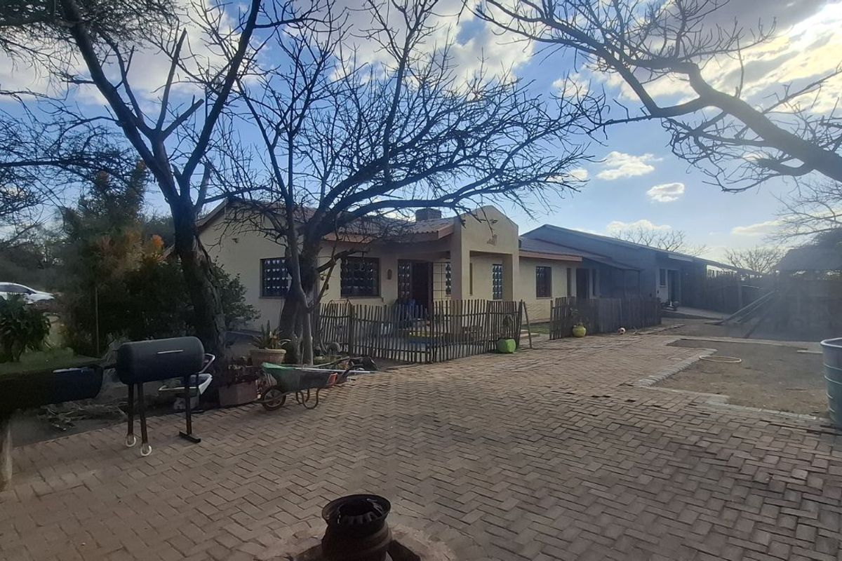 Spacious farm property featuring a paved courtyard area, established trees, and a functional outdoor living space with a built-in braai.