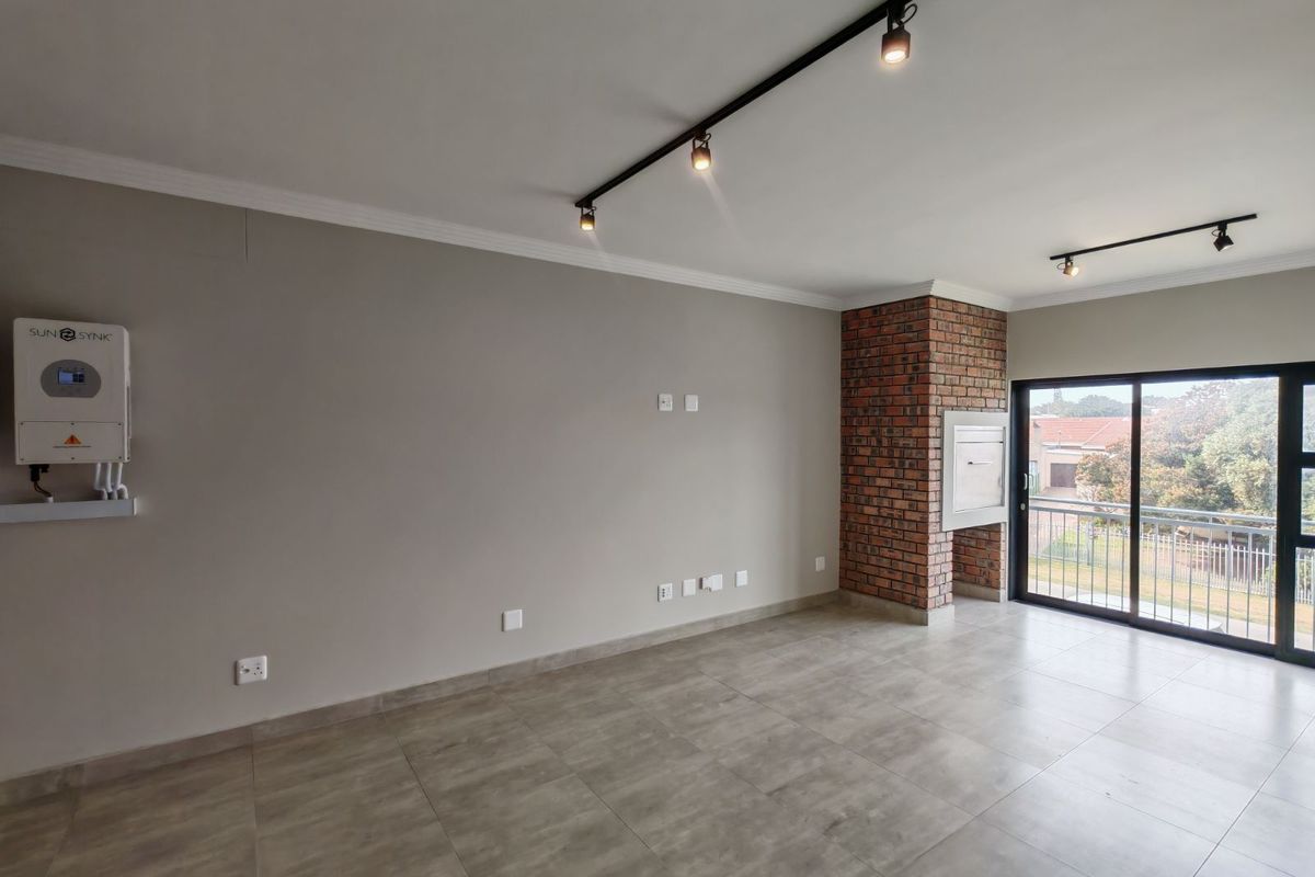Spacious living area featuring a built-in brick fireplace, modern track lighting, tiled flooring, and a Sunsynk inverter system, with access to a balcony.