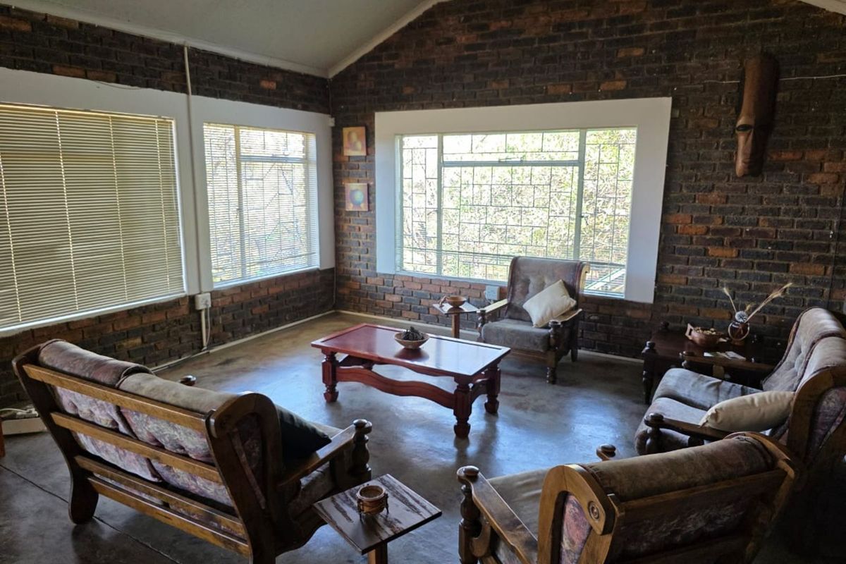A rustic living room featuring exposed face-brick walls, vaulted ceilings, and large windows that provide ample natural light and garden views.