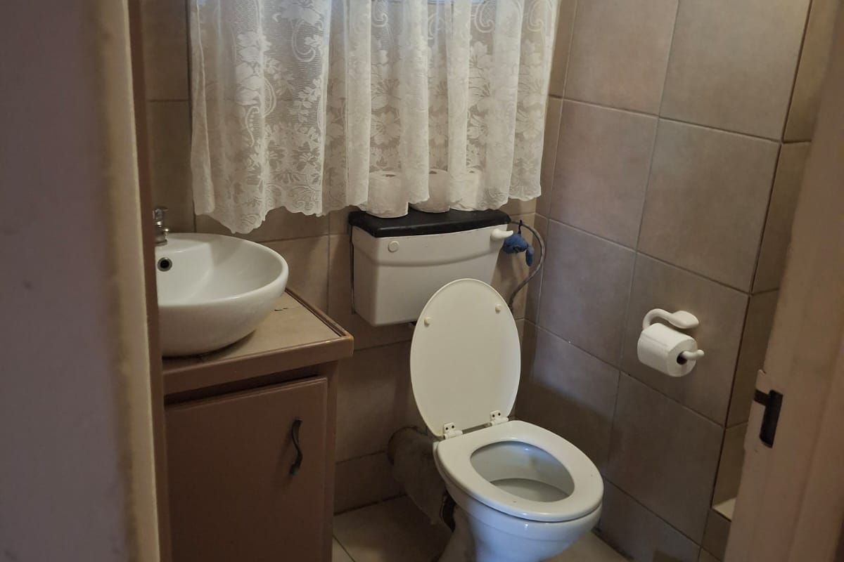 A compact bathroom featuring a vanity basin, toilet, and tiled walls, offering a functional layout in a neutral color palette.
