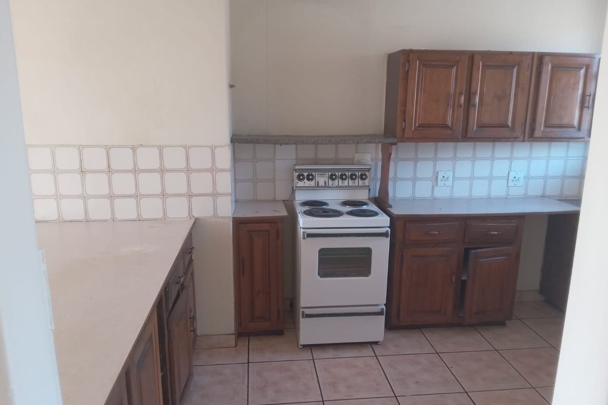 A dated kitchen featuring wooden cabinetry, a freestanding stove, tiled backsplash, and tiled flooring, offering a functional space ready for modernization.
