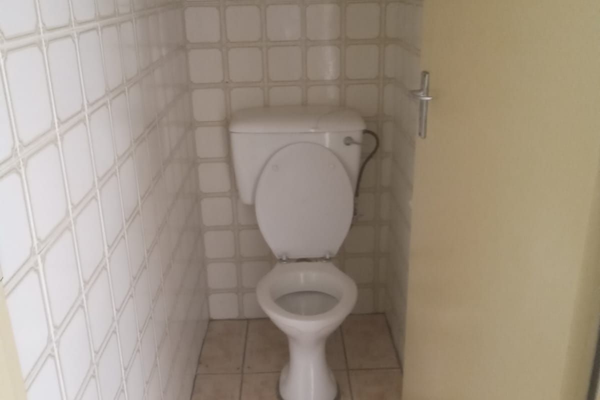 A compact, dated guest toilet featuring white wall tiles, ceramic floor tiles, and a small high-level window for ventilation.